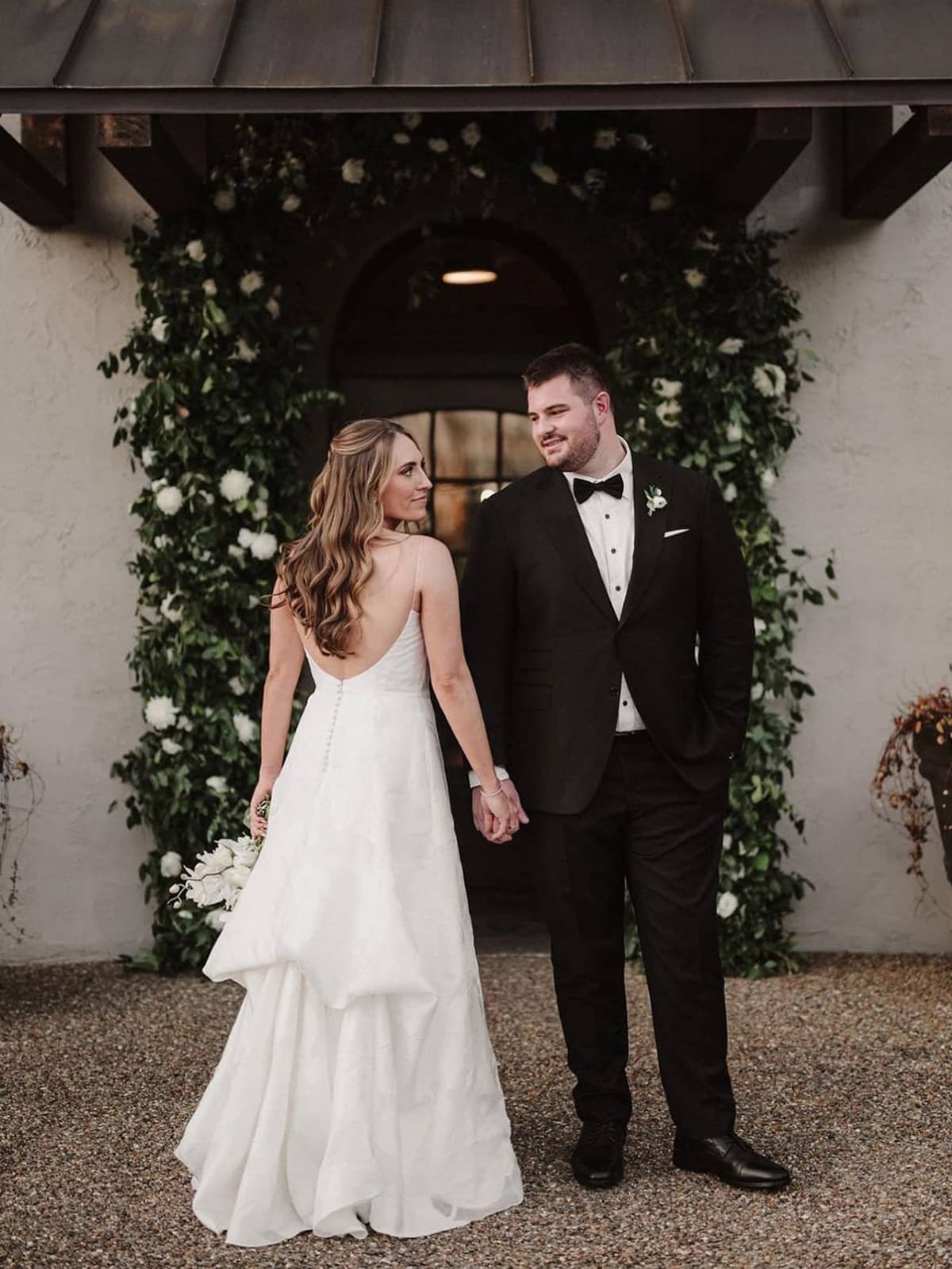 Landon Dickerson in a black tuxedo, holding hands with his bride outside their wedding venue