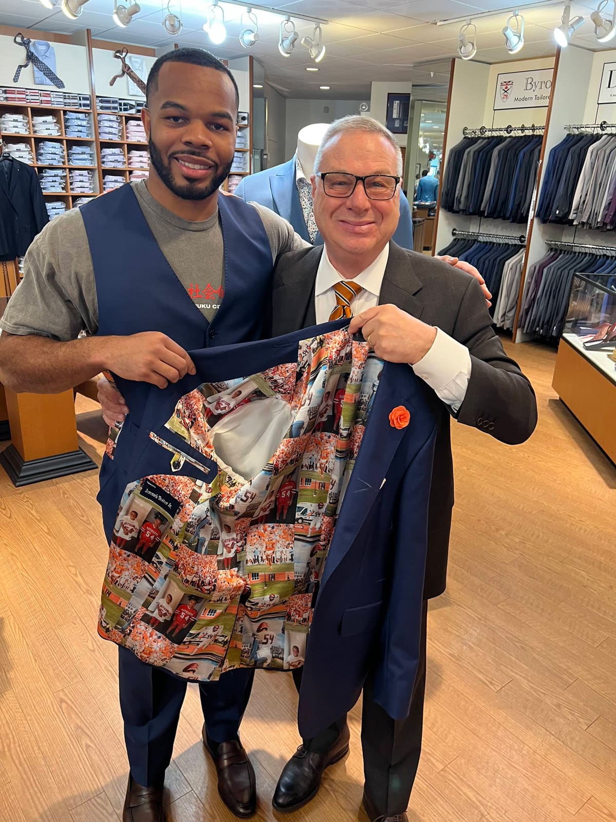 Jeremiah Trotter Jr. and a member of the Ventresca Ltd. team holding open a navy vest with a photo-printed lining