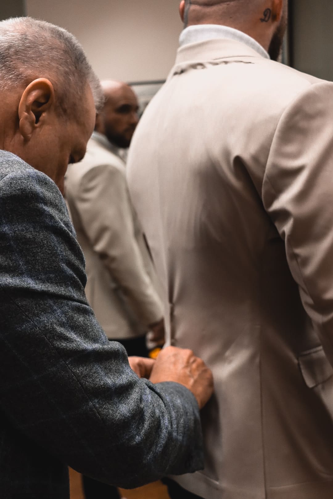 A tailor adjusting the back of a client's cream jacket in the store